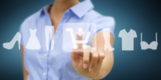 Une femme en blouse bleue touche un écran tactile affichant des icônes de vêtements et de chaussures, dans le cadre de ses achats en ligne.