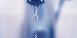 De dripping water uit een standaard kraan in een omgeving met blauwe tinten.