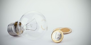 Une ampoule à côté de deux pièces d'un euro, symbolisant l'énergie et les coûts.