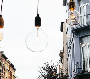 Trois lampes suspendues de différentes formes sont accrochées au-dessus d'une rue avec des bâtiments en arrière-plan.