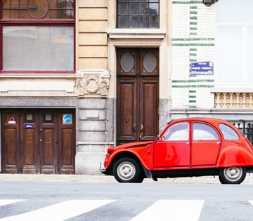 Voiture vintage rouge garée à côté d'un bâtiment historique avec des portes en bois et des carreaux.