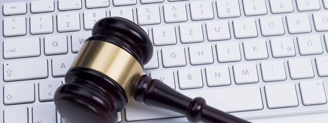 Un marteau repose sur un clavier d'ordinateur portable, symbolisant la combinaison du droit et de la technologie.