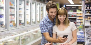Un couple regarde un smartphone tandis qu'il se tient devant les vitrines réfrigérées d'un supermarché.