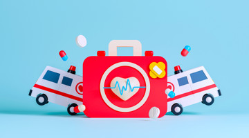 Trousse de secours pour enfants rouge avec un cœur et une croix, entourée de pilules en plastique et de deux ambulances jouet sur un fond bleu clair.